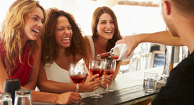 three women being poured wine by a bartender
